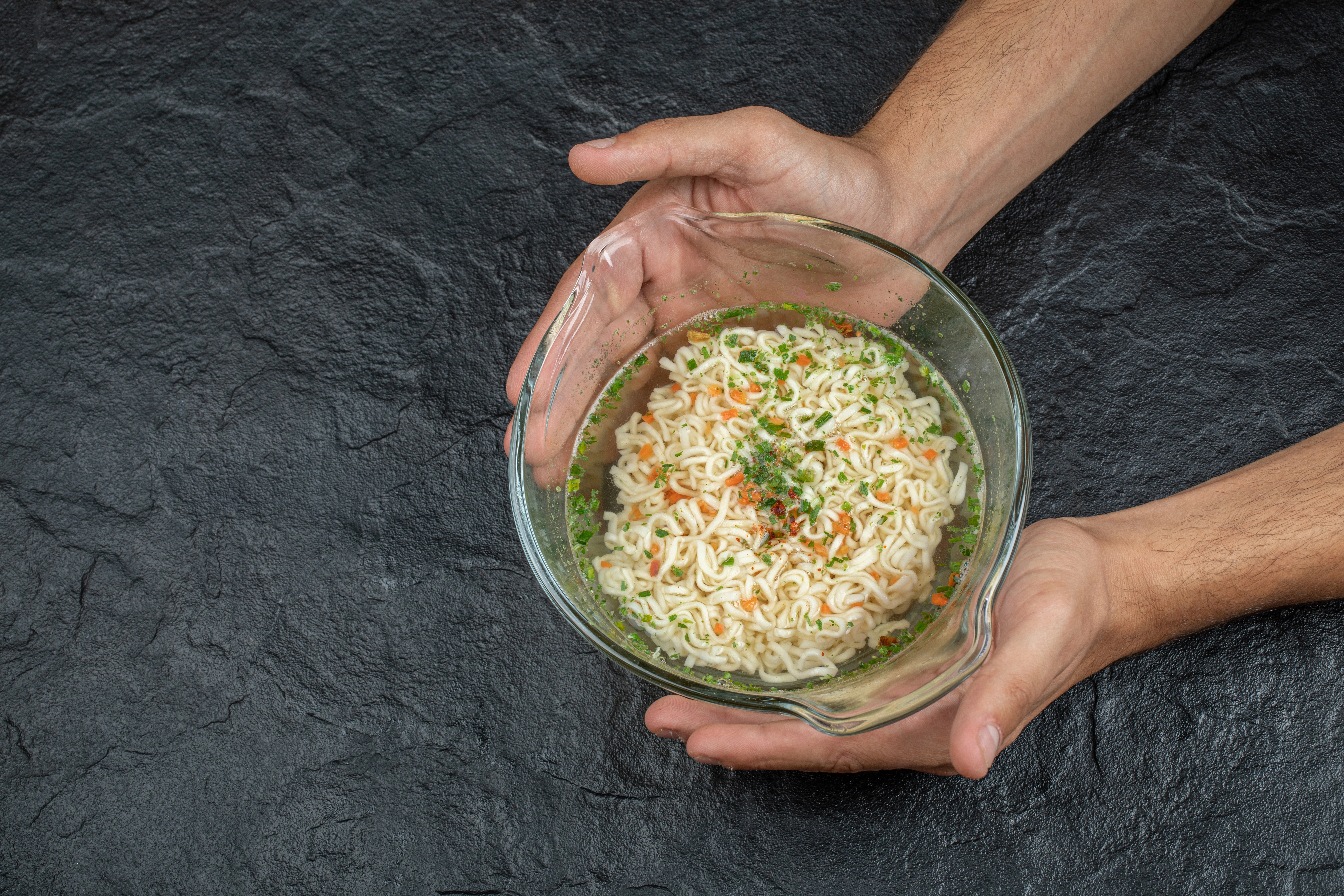 hands-holding-glass-plate-with-delicious-noodles-dark-surface.webp